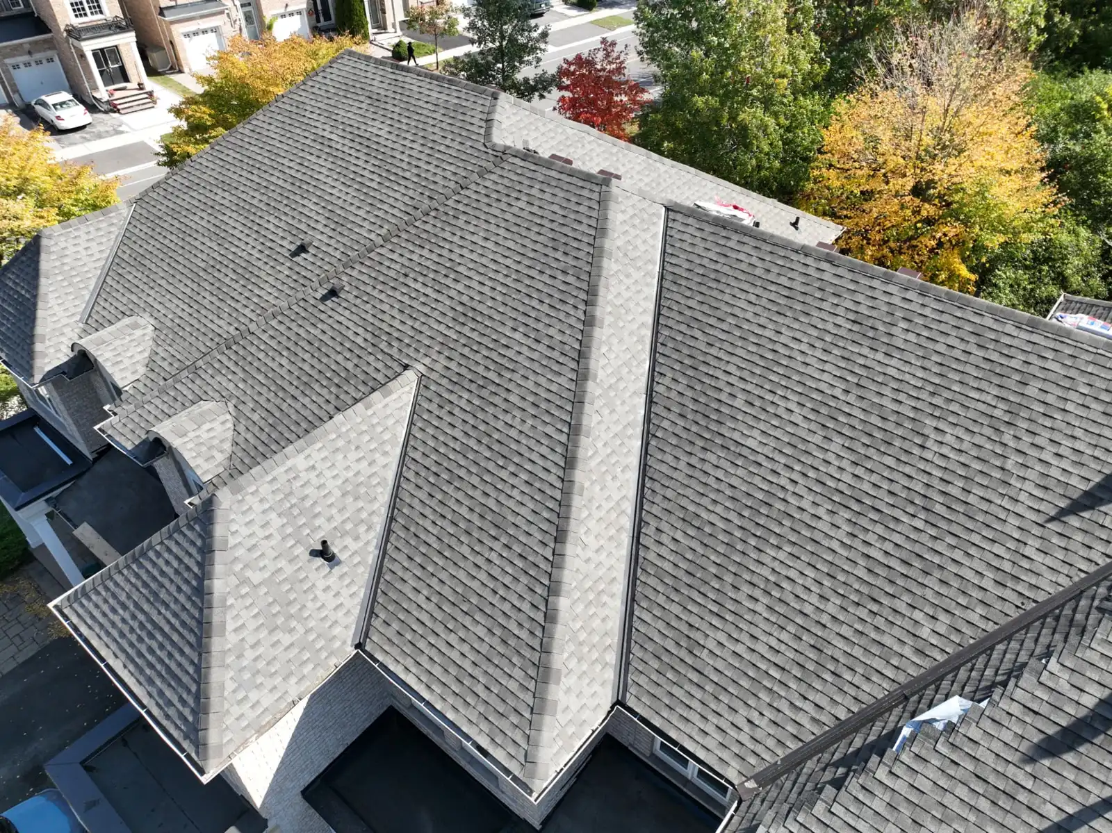 Drone view of the completed grey shingle roof on an Oakville home beside autumn trees