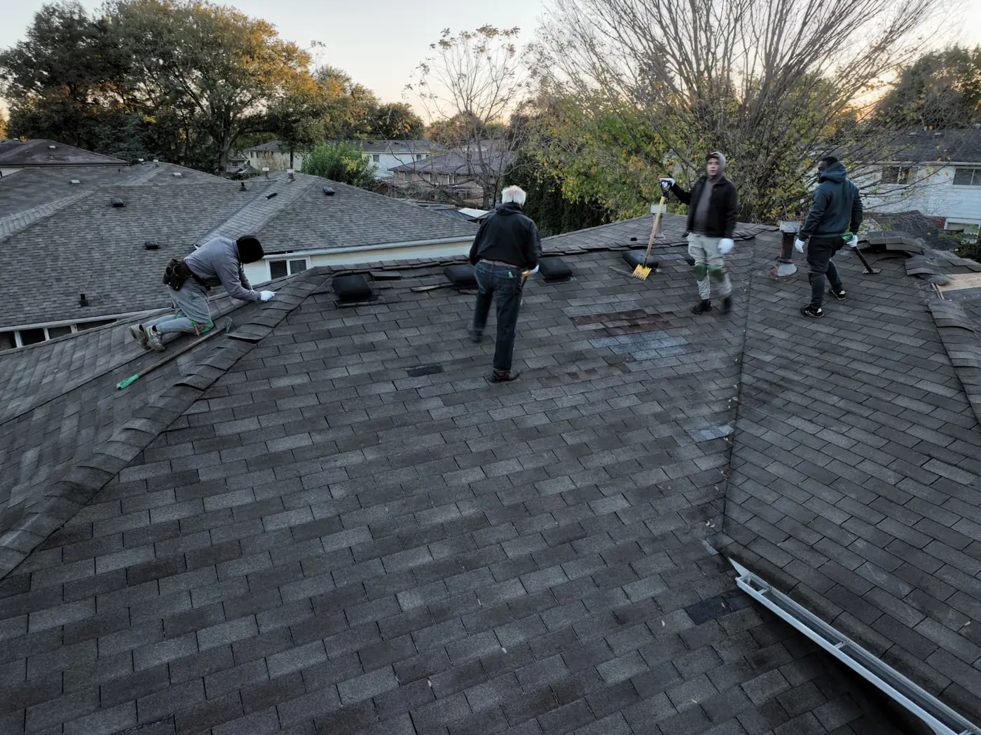 Drone view of the Ontario Tech Roofing crew working on a Mississauga shingle roof at dusk, removing old shingles with autumn trees and neighbouring homes behind