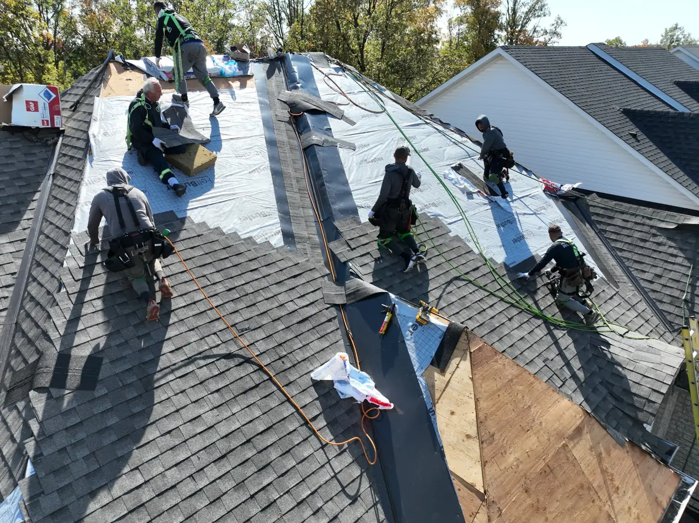 Close aerial view of Ontario Tech Roofing crew members installing shingles toward the ridge of an Oakville roof with material bundles staged nearby