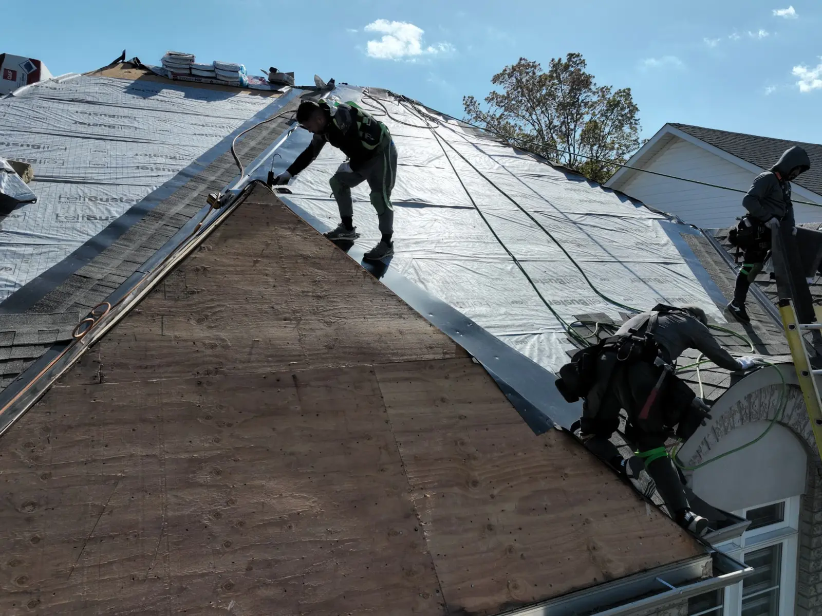 Oakville roofing crew working along a ridge above exposed plywood and silver underlayment