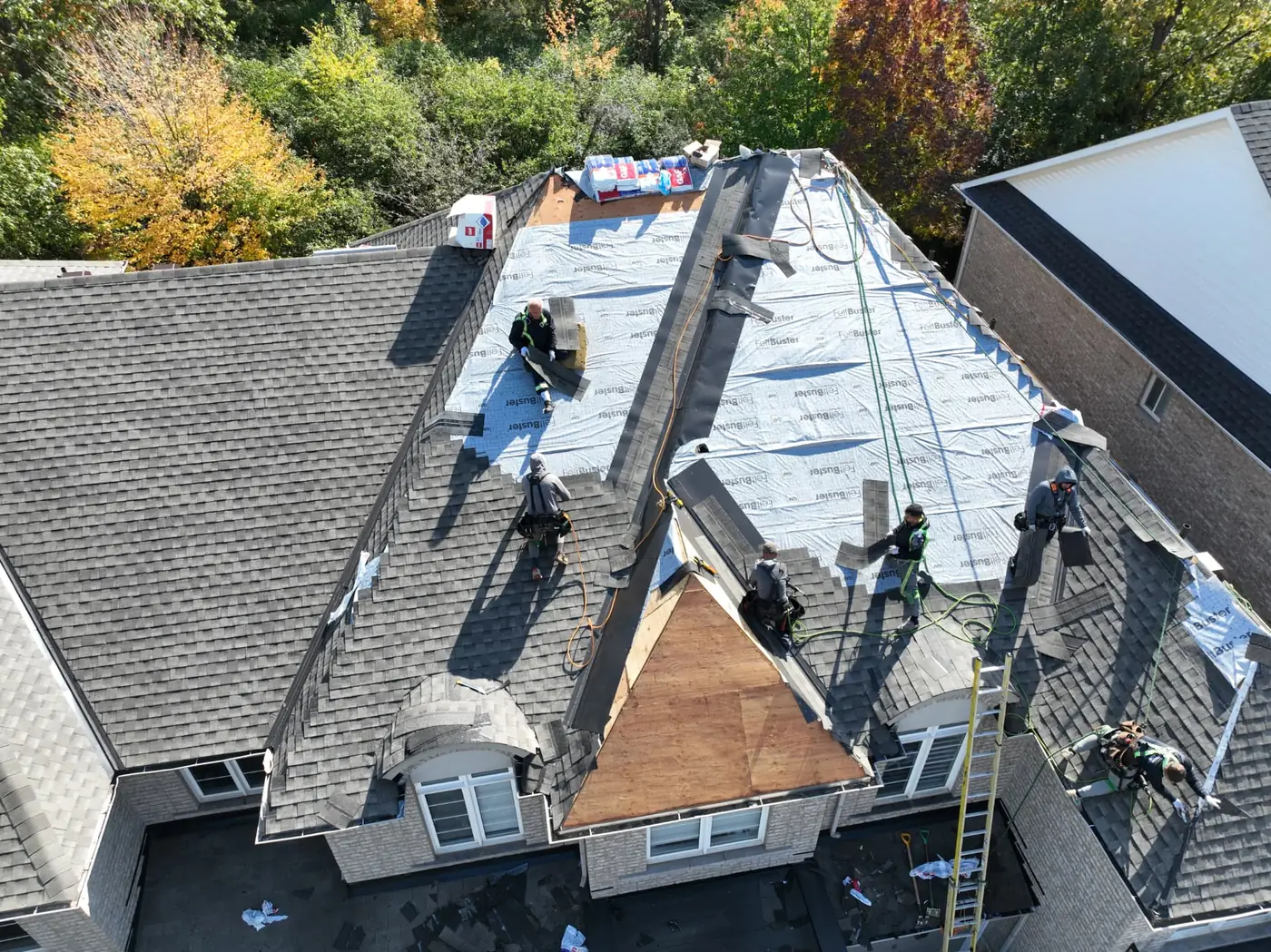 Overhead drone view of an Oakville roof replacement in progress, with synthetic underlayment strips, staged shingle bundles and several crew members at work