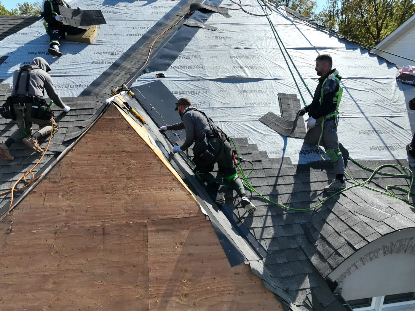 Crew members shingling around a hip on an Oakville roof with exposed plywood decking on the gable end and synthetic underlayment behind