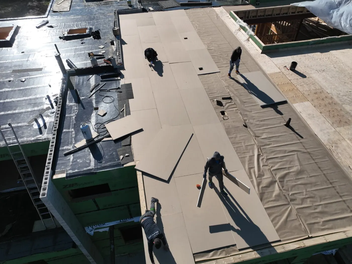 Aerial view of crew members fitting light-coloured rigid boards over a Brampton flat roof beside black membrane and exposed plywood decking