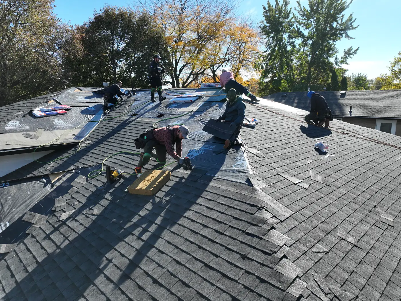 Roofers nailing new architectural shingles over black underlayment on a Hamilton home