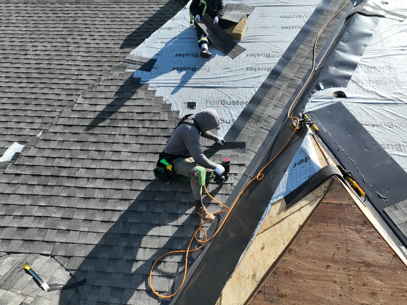 Top-down view of a roofer nailing shingles beside exposed plywood decking and synthetic underlayment on an Oakville roof