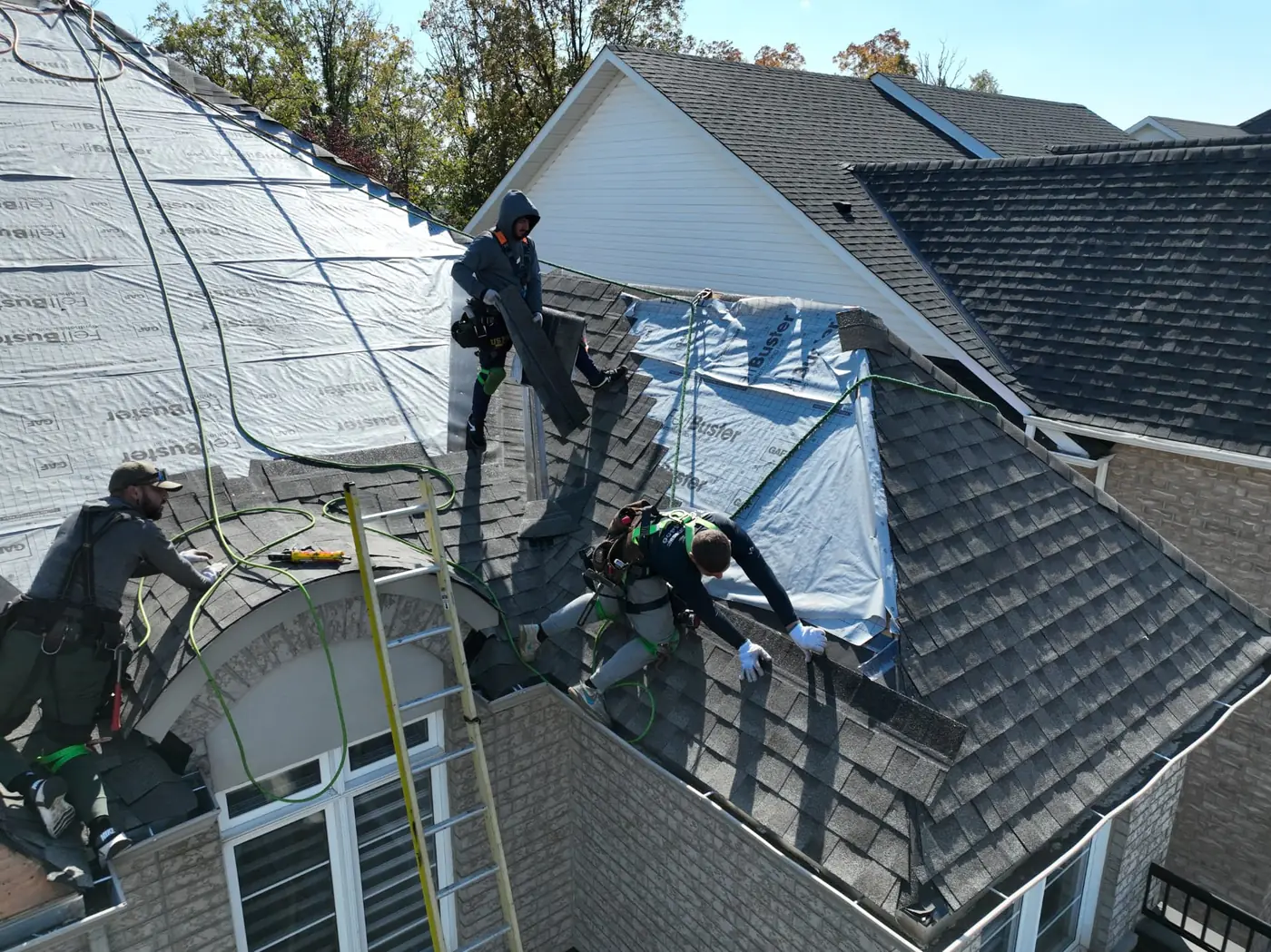 Aerial view of Ontario Tech Roofing crews installing grey shingles over synthetic underlayment on a large Oakville roof, with ladders against the front of the home