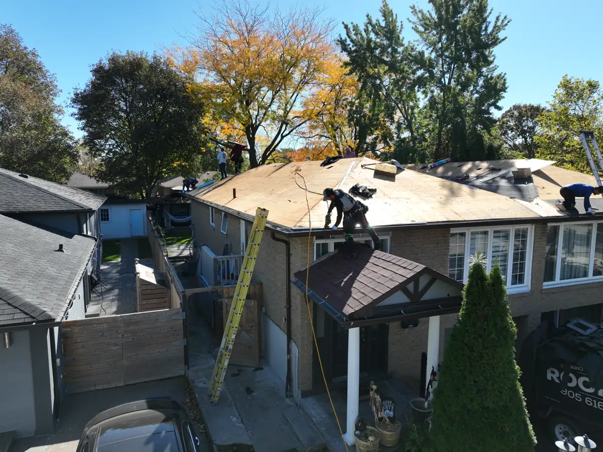Drone view of the Ontario Tech Roofing crew stripping a Mississauga semi-detached home down to the plywood decking, with ladders against the wall and the company truck in the driveway