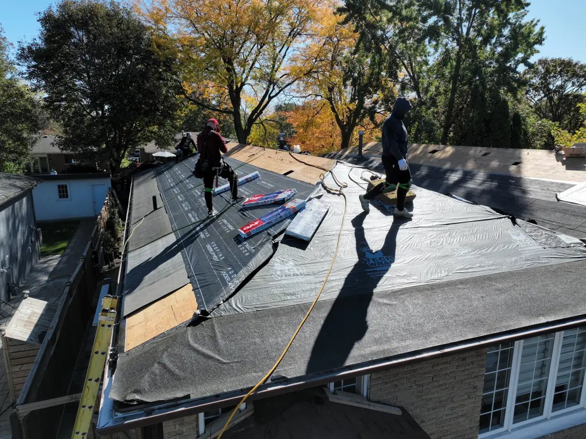 Roofers laying synthetic underlayment and GAF starter strips on a Mississauga roof, with autumn trees in the background