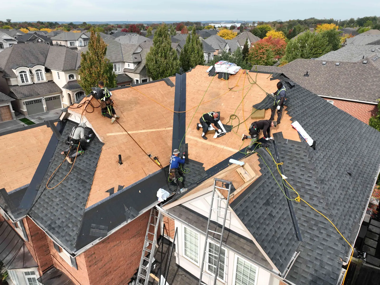 Aerial view of a steep Oakville roof partway through replacement, with exposed decking, new rows of shingles and two ladders against the gables
